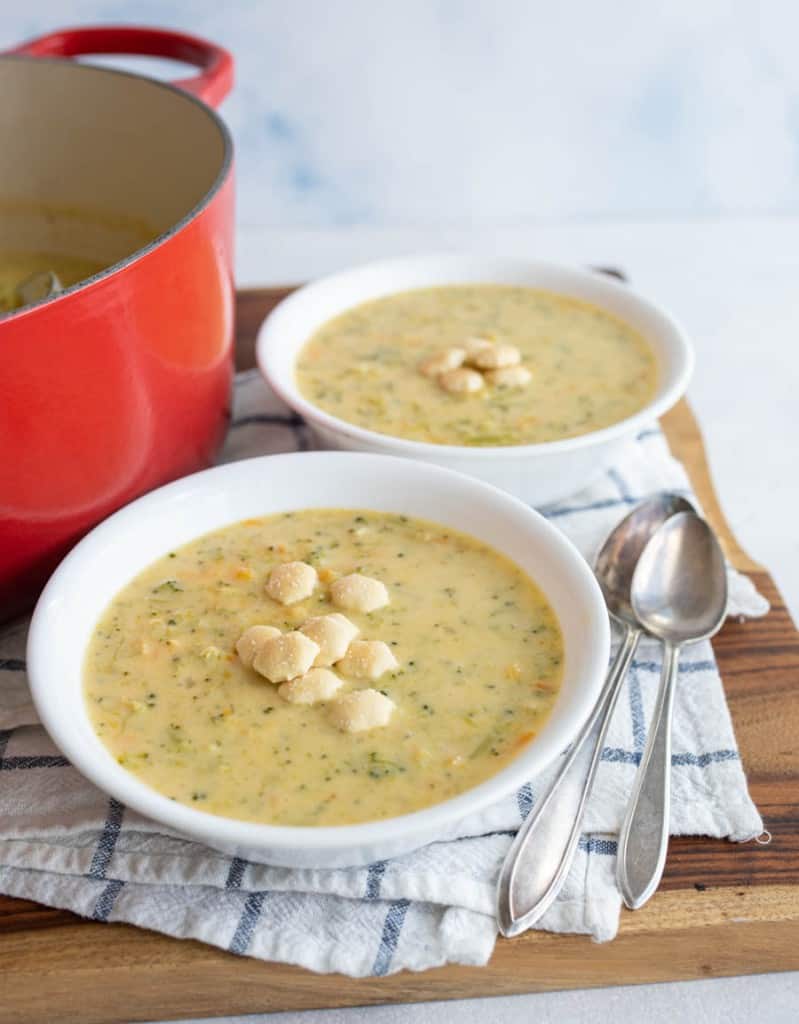 two white bowls and red dutch pot with cheddar broccoli soup and oyster crackers
