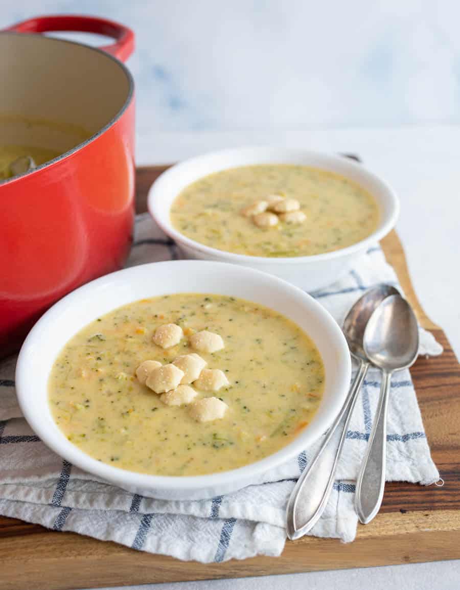 two white bowls and red dutch pot with cheddar broccoli soup and oyster crackers