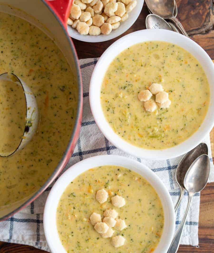 top view of two white bowls and red dutch pot with cheddar broccoli soup and oyster crackers