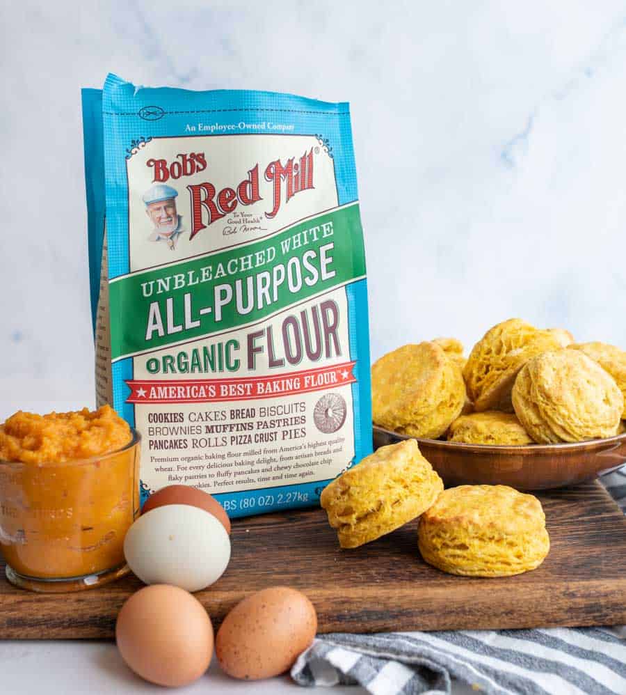 bag of flour, pumpkin puree in glass dish, and colored chicken eggs on a cutting board