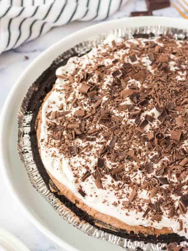 A chocolate cream pie with a whipped topping and chocolate shavings in a foil pie pan, placed on a white plate.