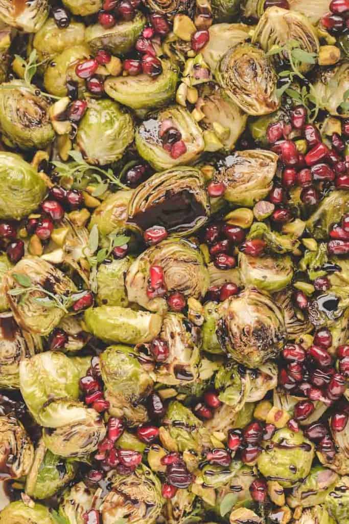 Roasted Brussels sprouts in the oven are topped with pomegranate seeds, pistachios, and fresh herbs, creating a colorful and vibrant dish with a delightful mix of green, red, and brown tones.
