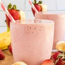 strawberry banana smoothies in cups with pink striped paper straws and fresh fruit all around