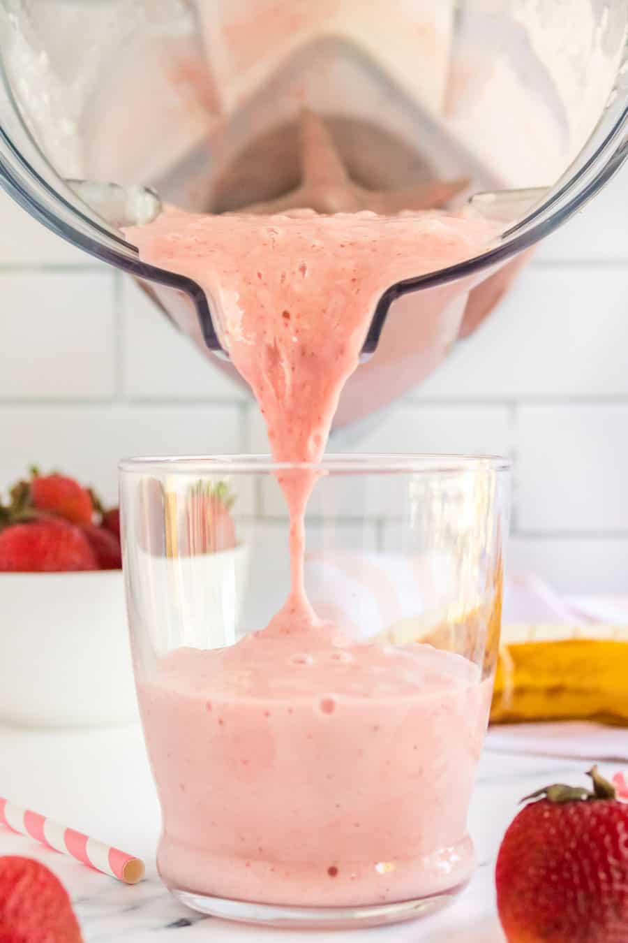 strawberry banana smoothies in cups with pink striped paper straws and fresh fruit all around