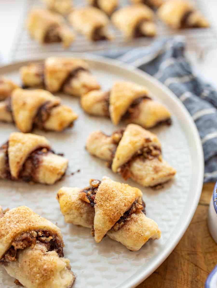 rugelach cookies on a large round plate, which look like stuffed and gooey rustic croissants