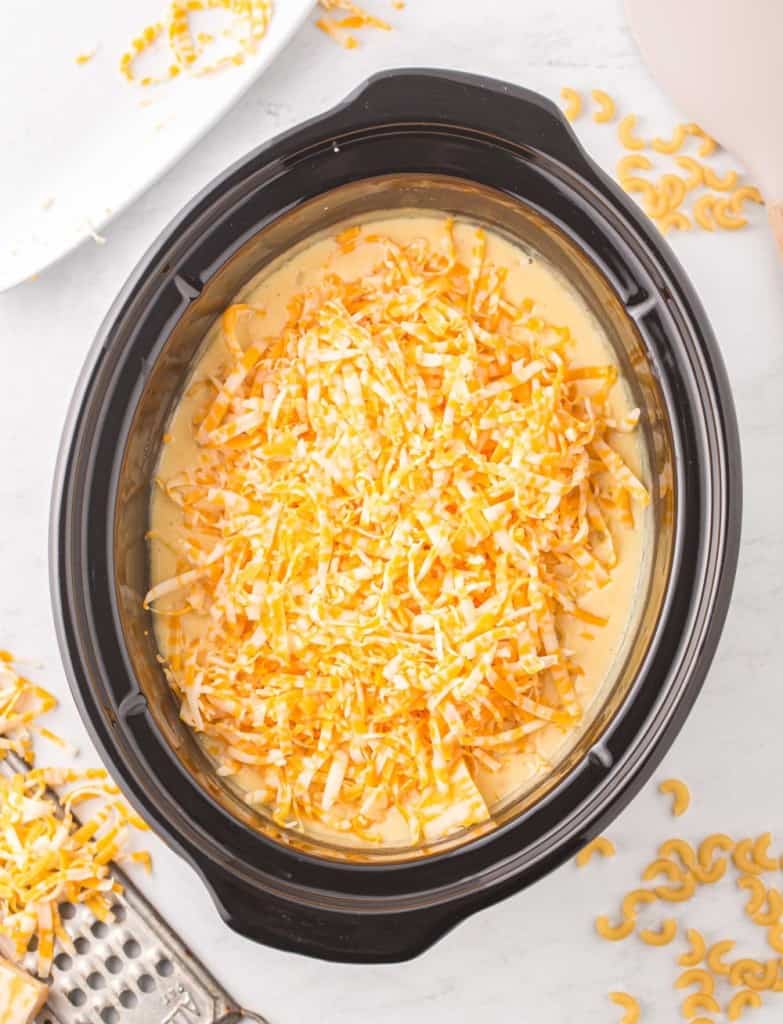 shredded cheese blend on top of a creamy sauce in a crock pot