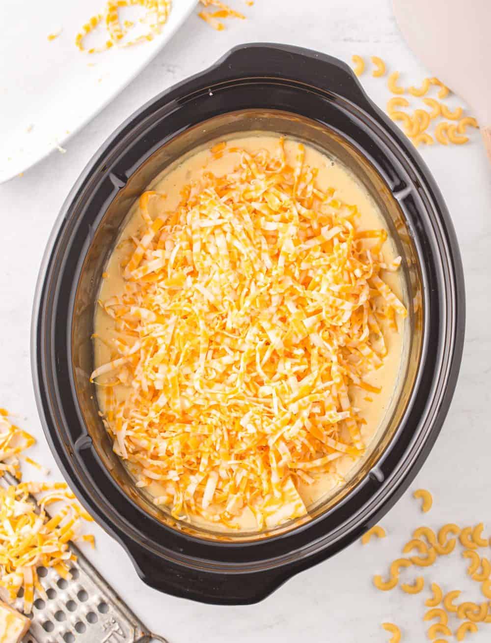 shredded cheese blend on top of a creamy sauce in a crock pot