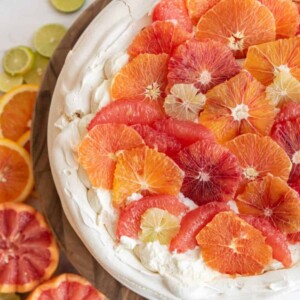 whole citrus pavlova in a vibrant display of decorative orange, blood orange, and lime cut out to decorate