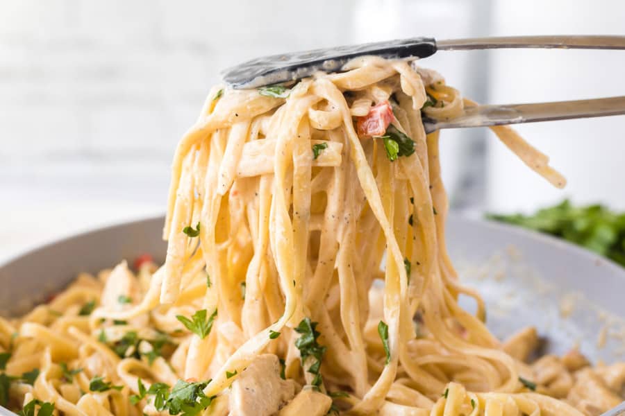 cajun chicken pasta between tongs being lifted from the pan