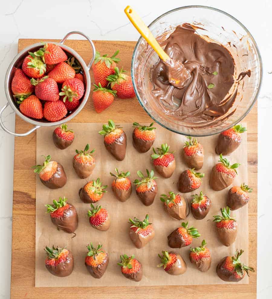 chocolate covered strawberries on parchment paper with a bowl of chocolate