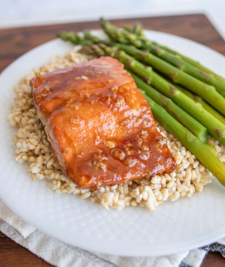 honey glazed salmon dinner on a plate over rice with asparagus as a side