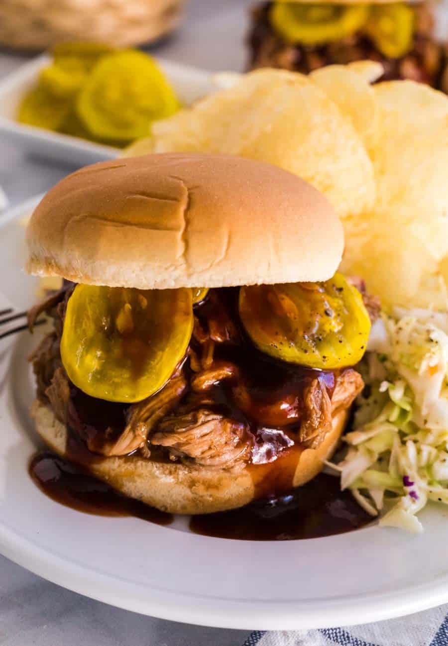 barbecue pulled pork sandwich on a plate with slaw and chips