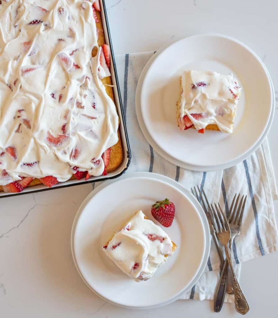 top view of a sheet pan strawberry shortcake and two servings dished onto white plates
