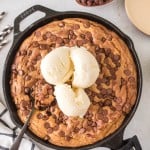 cast iron skillet with a big pizza shaped chocolate chip cookie with vanilla ice cream on top