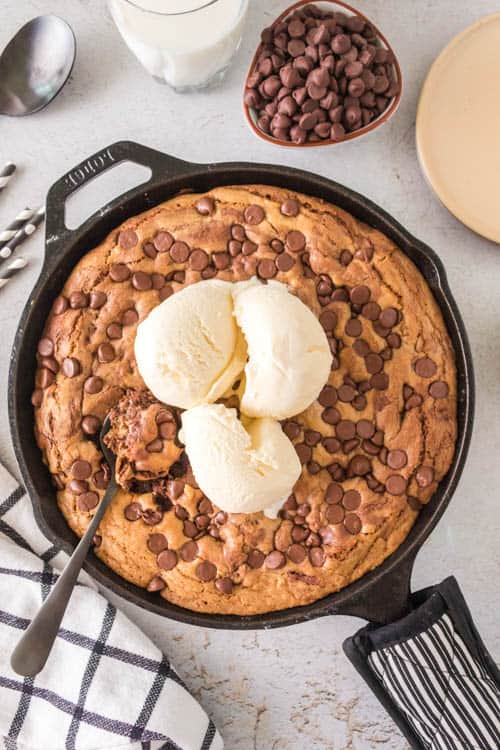 cast iron skillet with a big pizza shaped chocolate chip cookie with vanilla ice cream on top