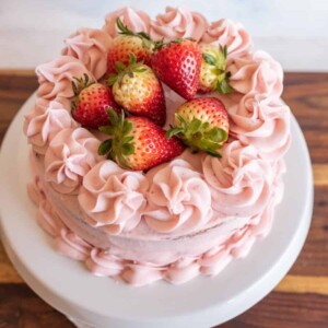 whole pink strawberry cake with strawberry buttercream and whole strawberries on top