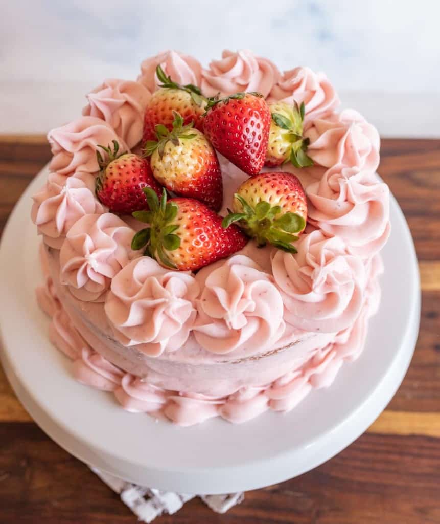 whole pink strawberry cake with strawberry buttercream and whole strawberries on top