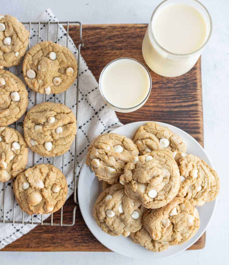 row of macadamia white chocolate chip cookies on cooling rack and some piled on a plate with milk to the side