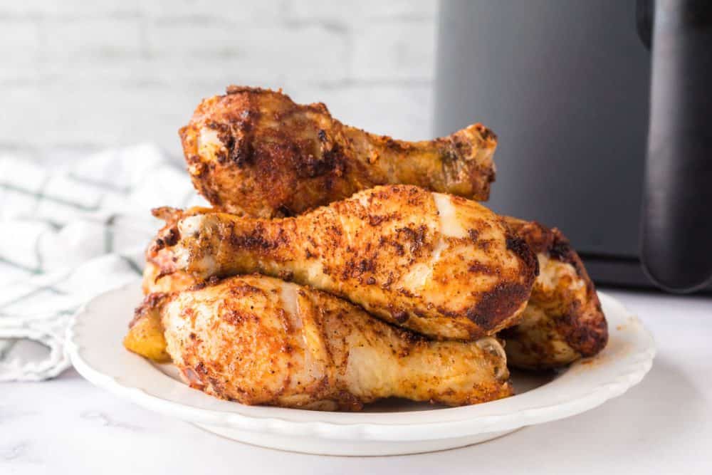 air fryer chicken legs and their crispy brown skin stacked on a white plate.