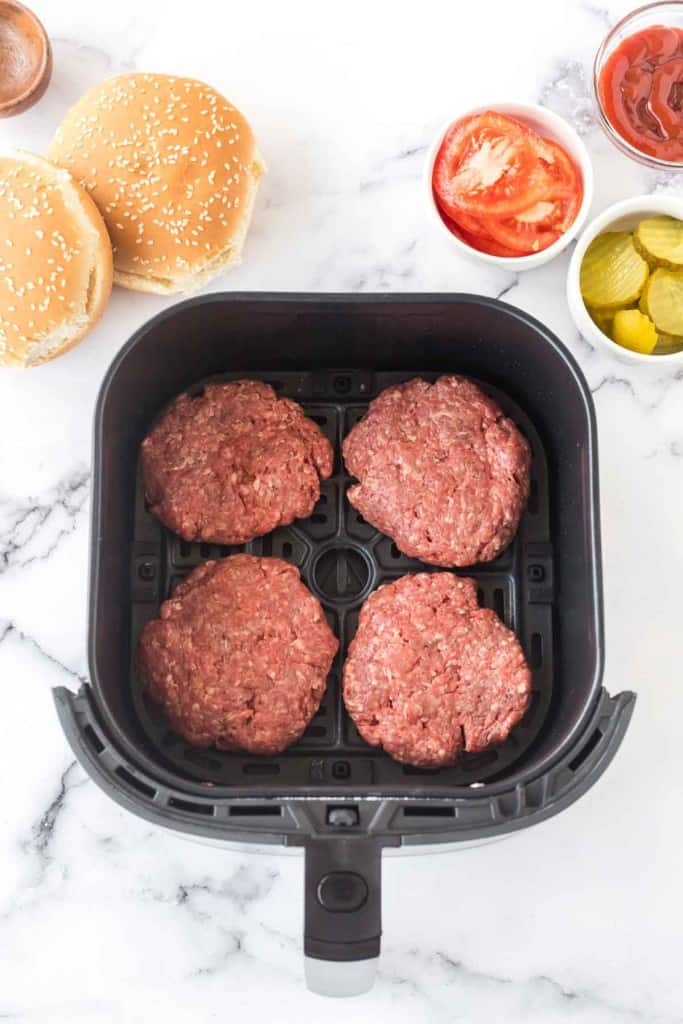 air fryer with four raw hamburger patties
