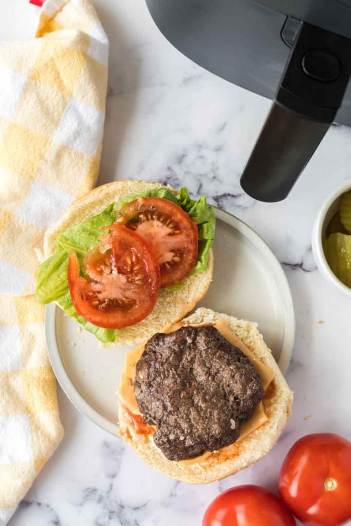 top view of an air fryer hamburger on a white plate open face with tomatoes and lettuce