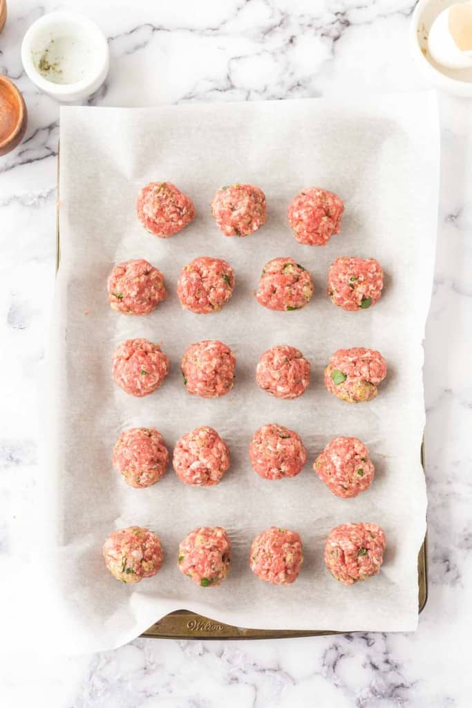 raw meatballs shaped into rows on parchment on a baking dish