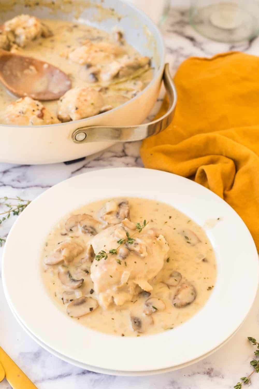 white bowl of chicken fricassee with the simmering pan in the background