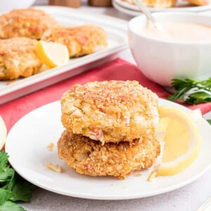 Two crab cakes stacked on top of each other with a platter of crab cakes in the background.