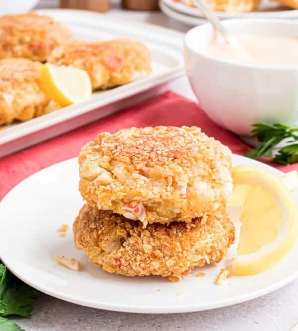 Two crab cakes stacked on top of each other with a platter of crab cakes in the background.