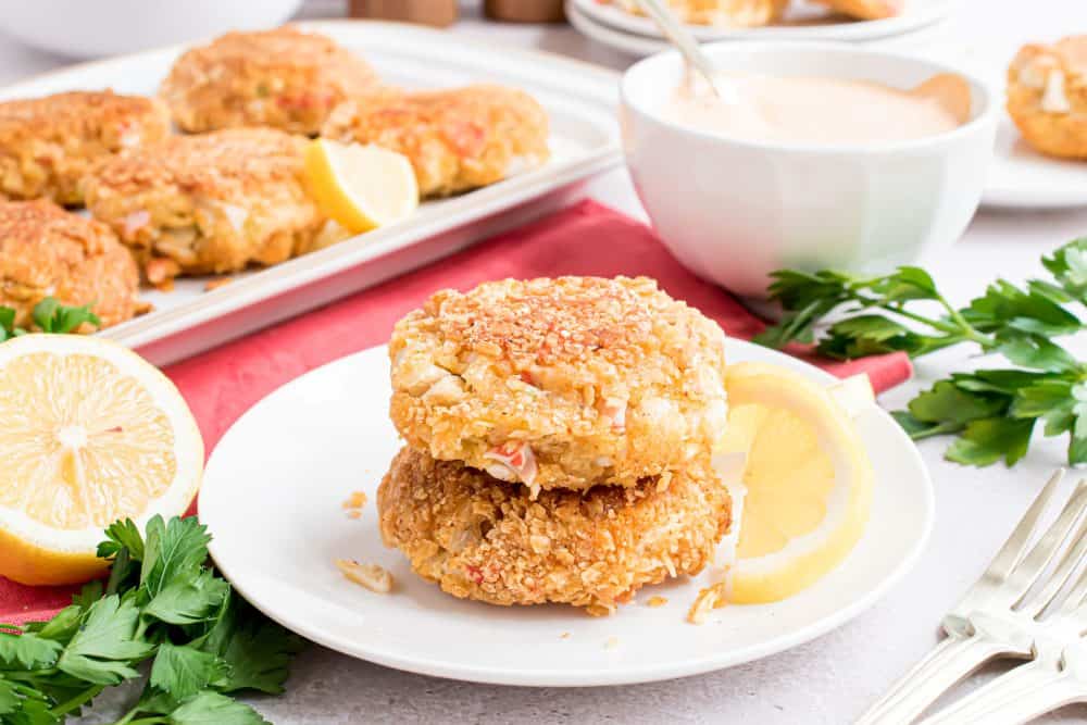 Two crab cakes stacked on top of each other with a platter of crab cakes in the background. 