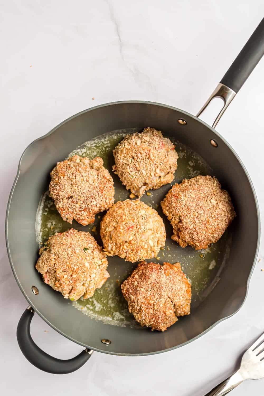 Crab cakes cooking in a skillet.