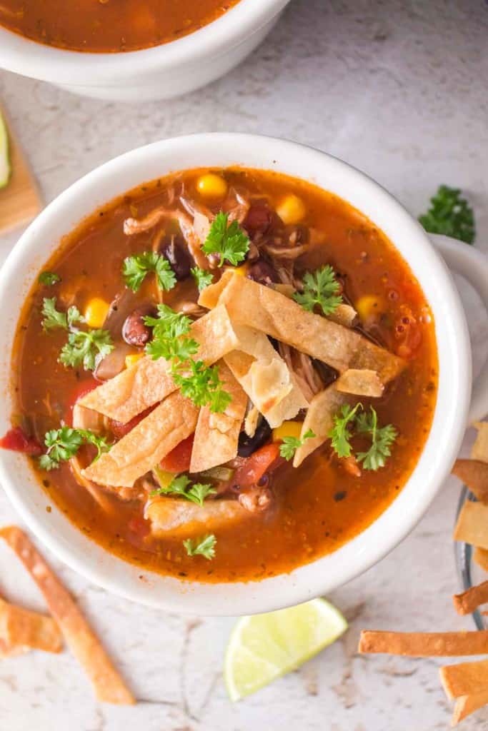a white bowl with chicken tortilla soup and sliced chips and cheese on top