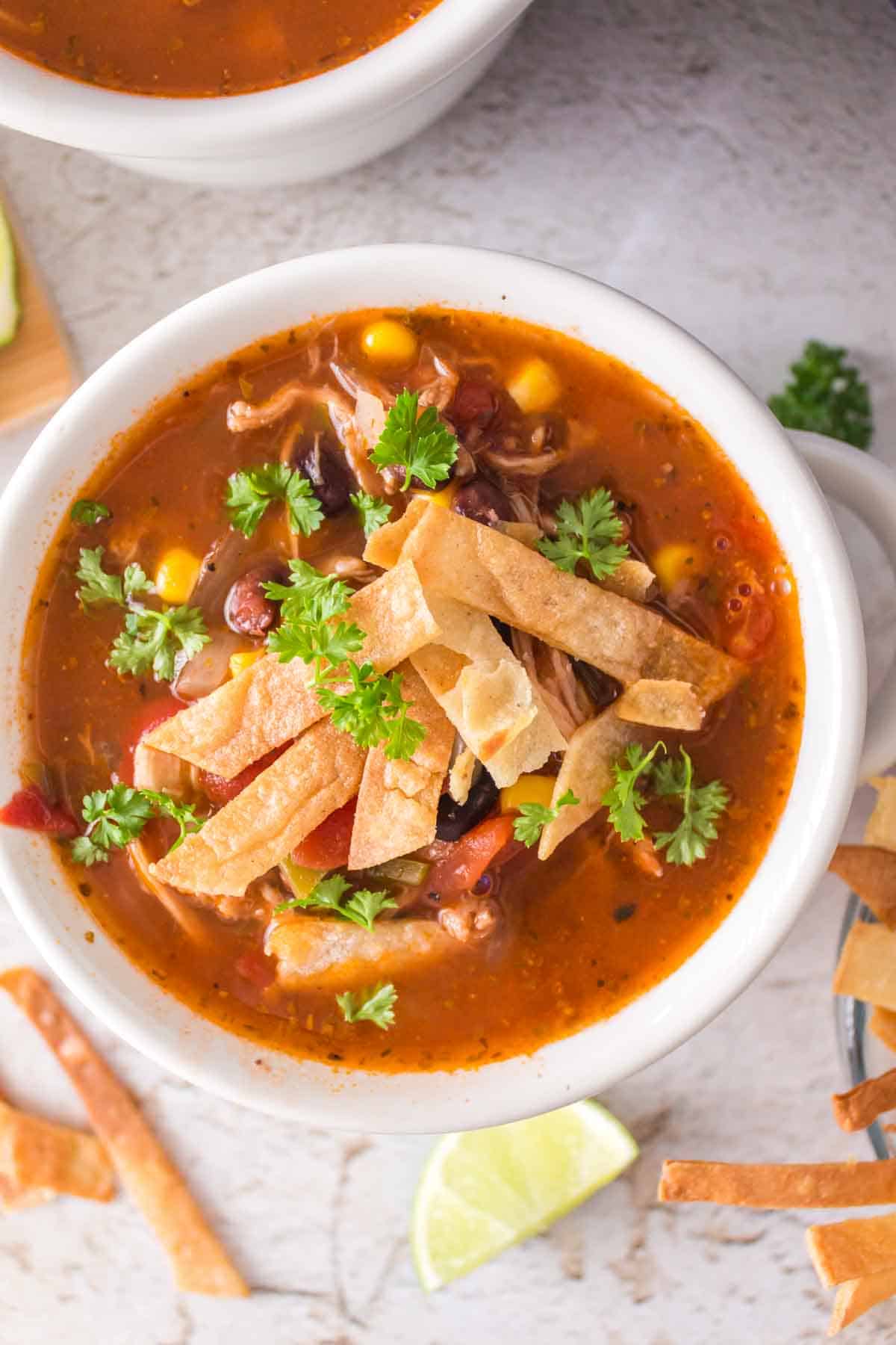 a white bowl with chicken tortilla soup and sliced chips and cheese on top