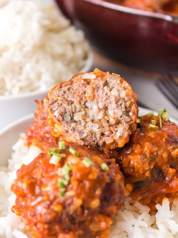 close up of porcupine meatballs with sauce over rice cut in half to reveal the inside
