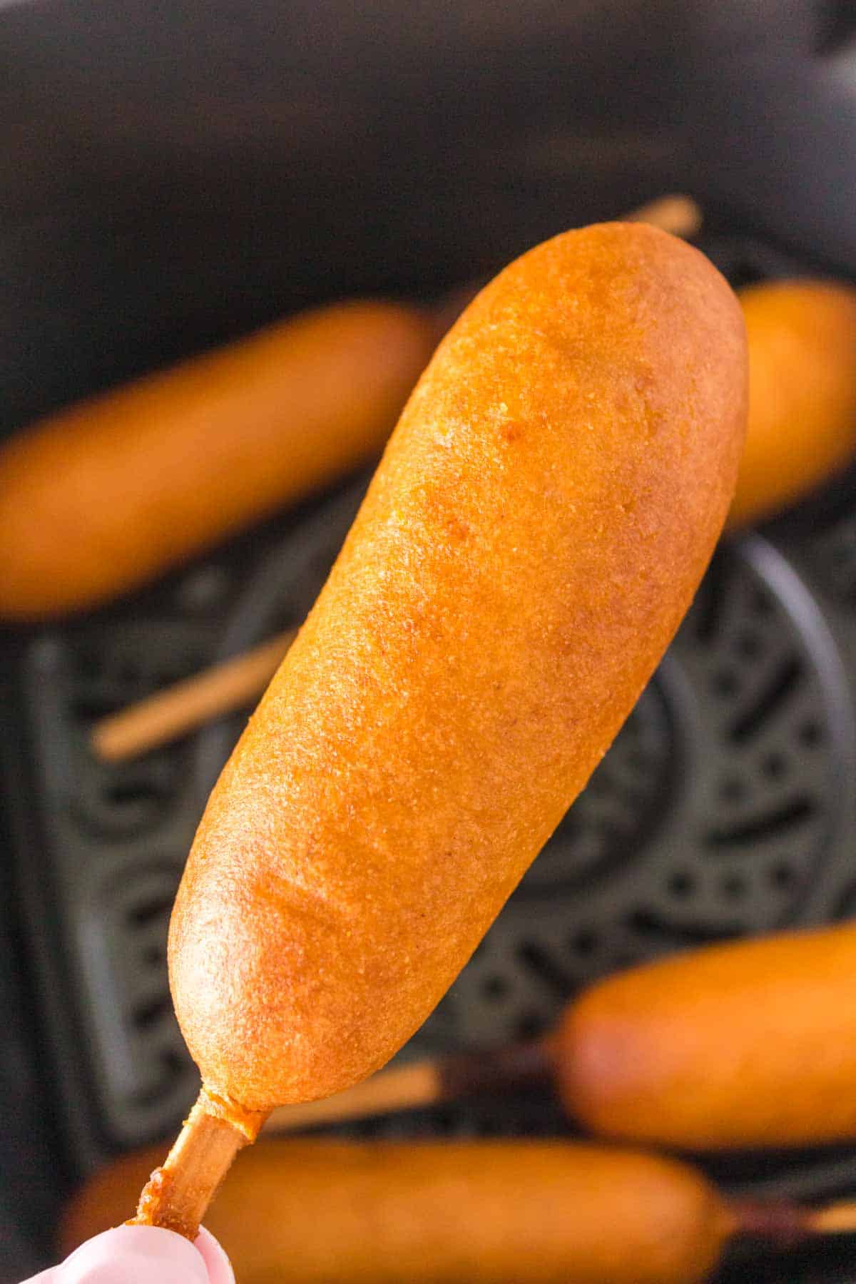 air fryer corn dogs lined up in the basket POV hand holding one up close
