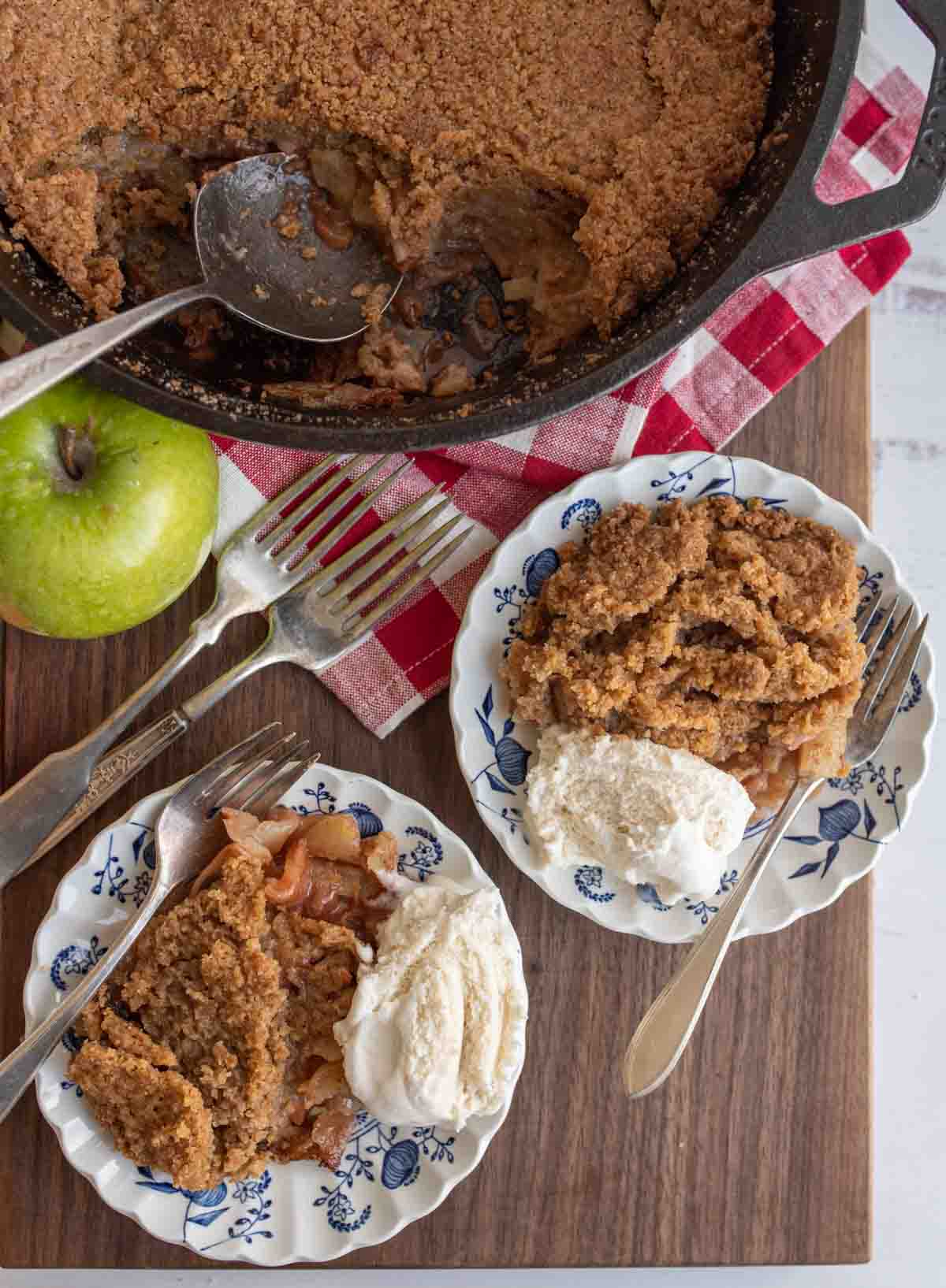 apple crumble served on plates with ice cream and the whole crumble in a cast iron pan