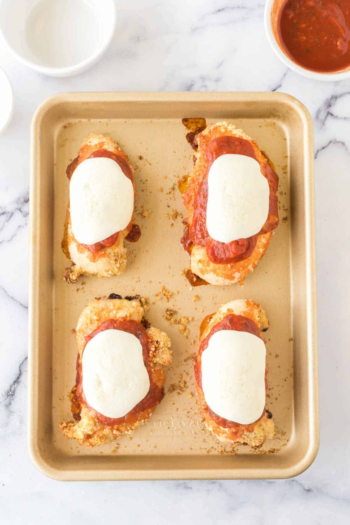 Four parmesan chicken breasts on a baking sheet.