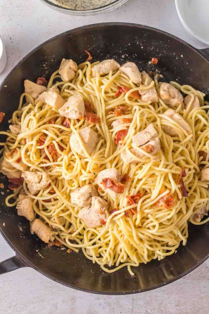 Chicken and bacon added to a pan of noodles for chicken carbonara.