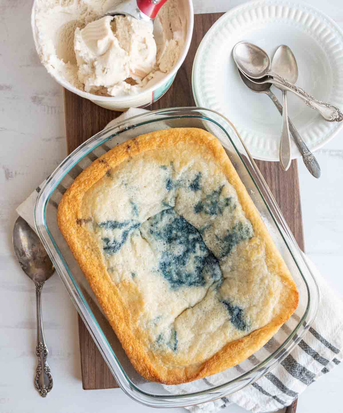 easy blueberry cobbler portioned onto plates with ice cream next to the clear baking dish