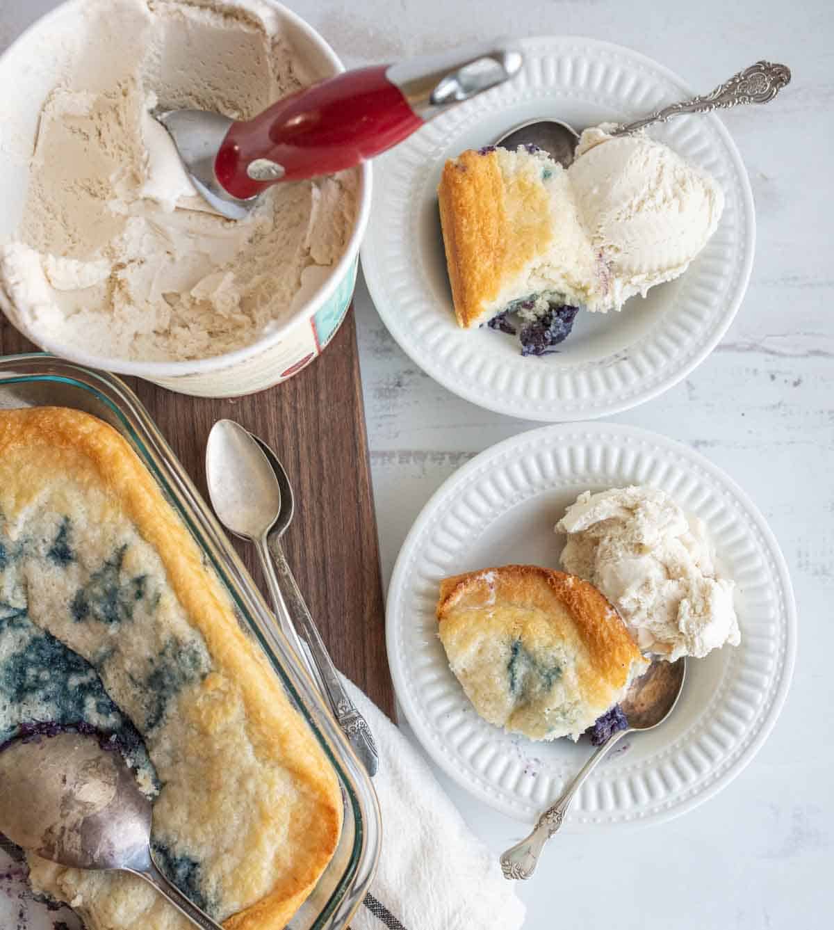 easy blueberry cobbler portioned onto plates with ice cream next to the clear baking dish