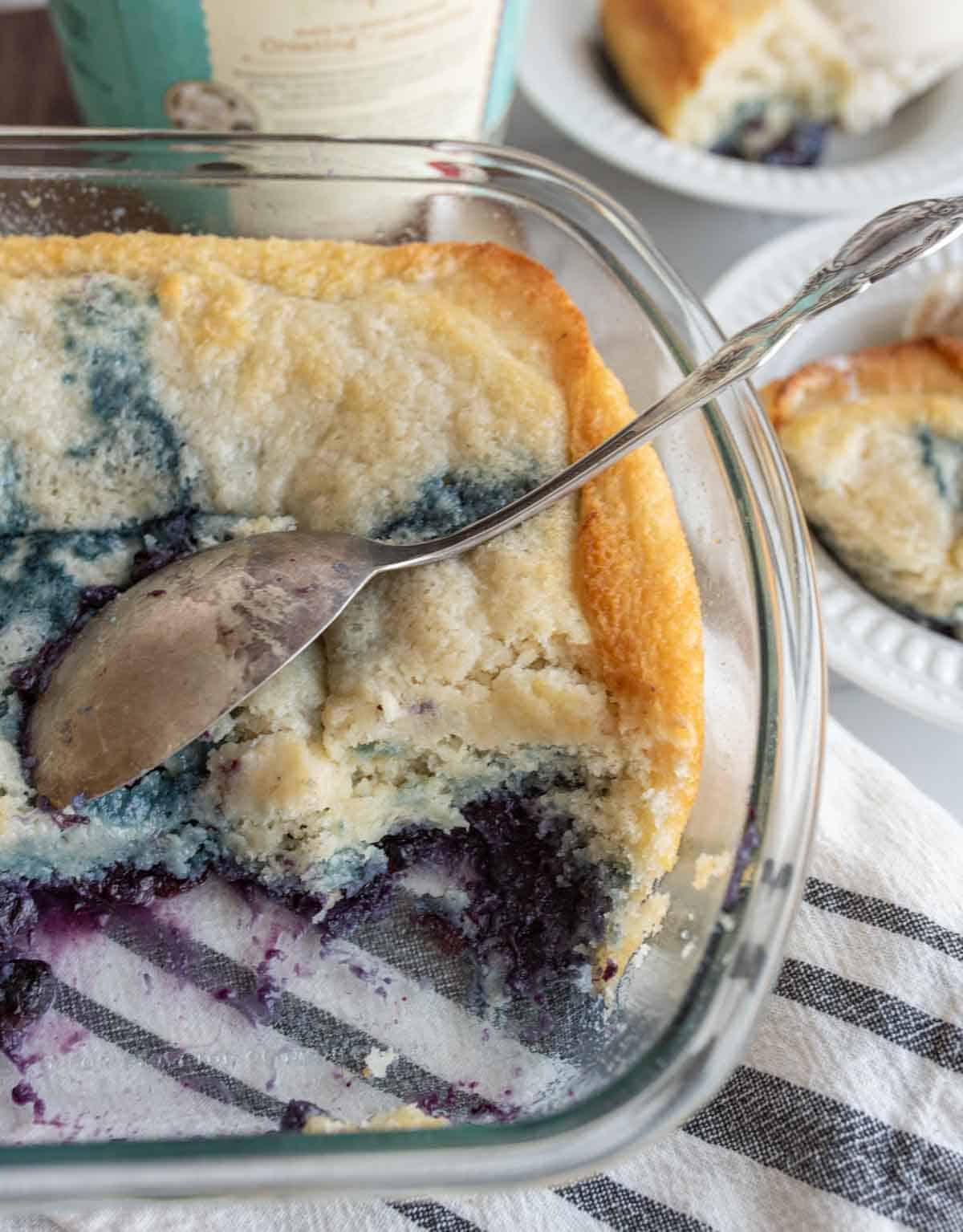 easy blueberry cobbler portioned onto plates with ice cream next to the clear baking dish