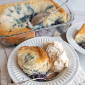 easy blueberry cobbler portioned onto plates with ice cream next to the clear baking dish