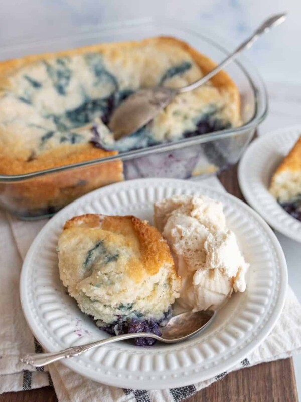 easy blueberry cobbler portioned onto plates with ice cream next to the clear baking dish