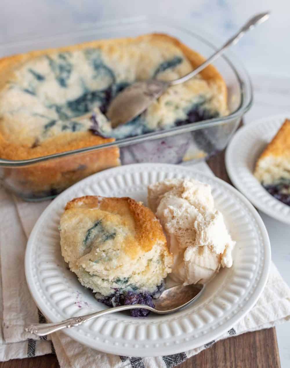 easy blueberry cobbler portioned onto plates with ice cream next to the clear baking dish