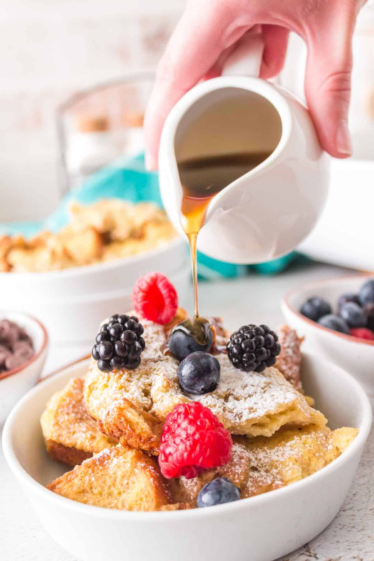 french toast bake with a serving dished onto a plate with powdered sugar berries and syrup