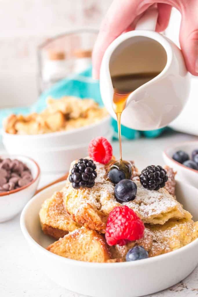 french toast bake with a serving dished onto a plate with powdered sugar berries and syrup