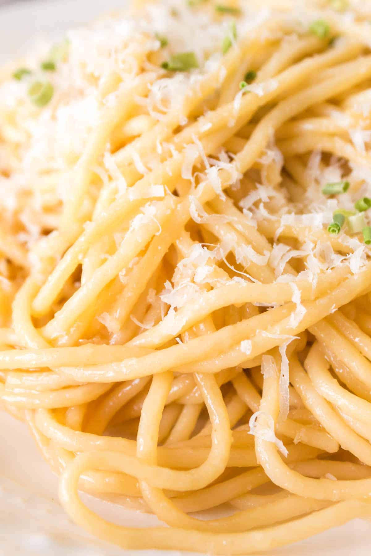 close up of a white plate of garlic noodle dinner with cheese and herbs on top