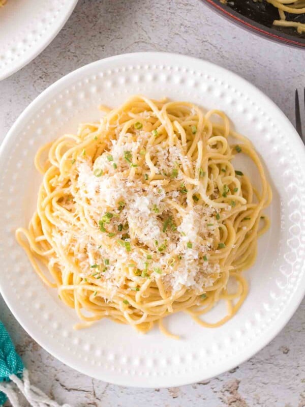 white plate of garlic noodle dinner with cheese and herbs on top
