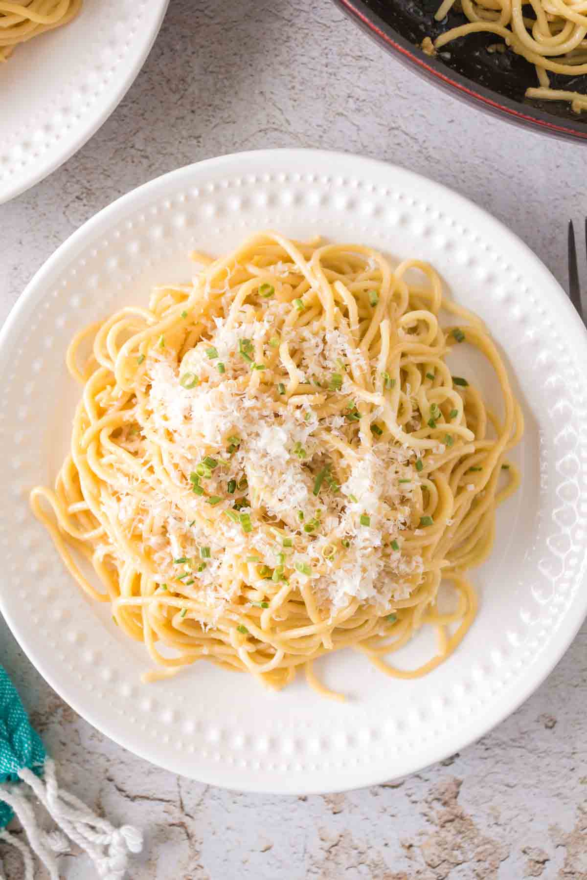 white plate of garlic noodle dinner with cheese and herbs on top