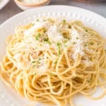 white plate of garlic noodle dinner with cheese and herbs on top